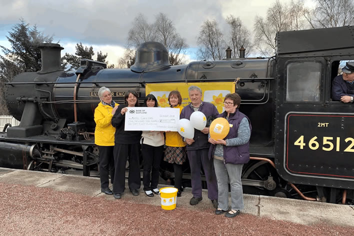 Marie Curie Lunch group standing infront of Ivatt locomotive 46512 E V Cooper Engineer at Platform 3 Aviemore railway station